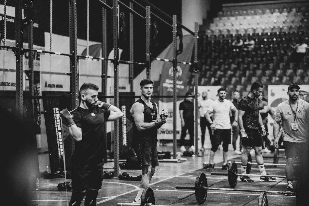 Sportifs de CrossFit entre deux épreuves, barres au sol, dans une salle de compétition